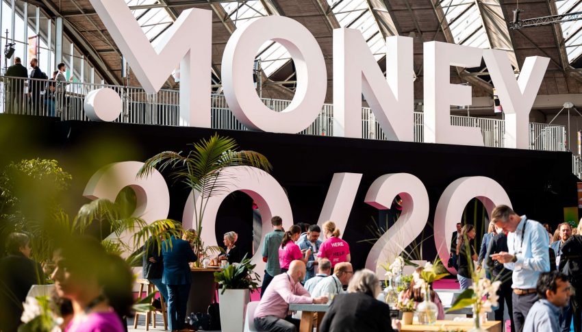 A photograph of the large Money 20/20 sign, with chatting delegates surrounding it.