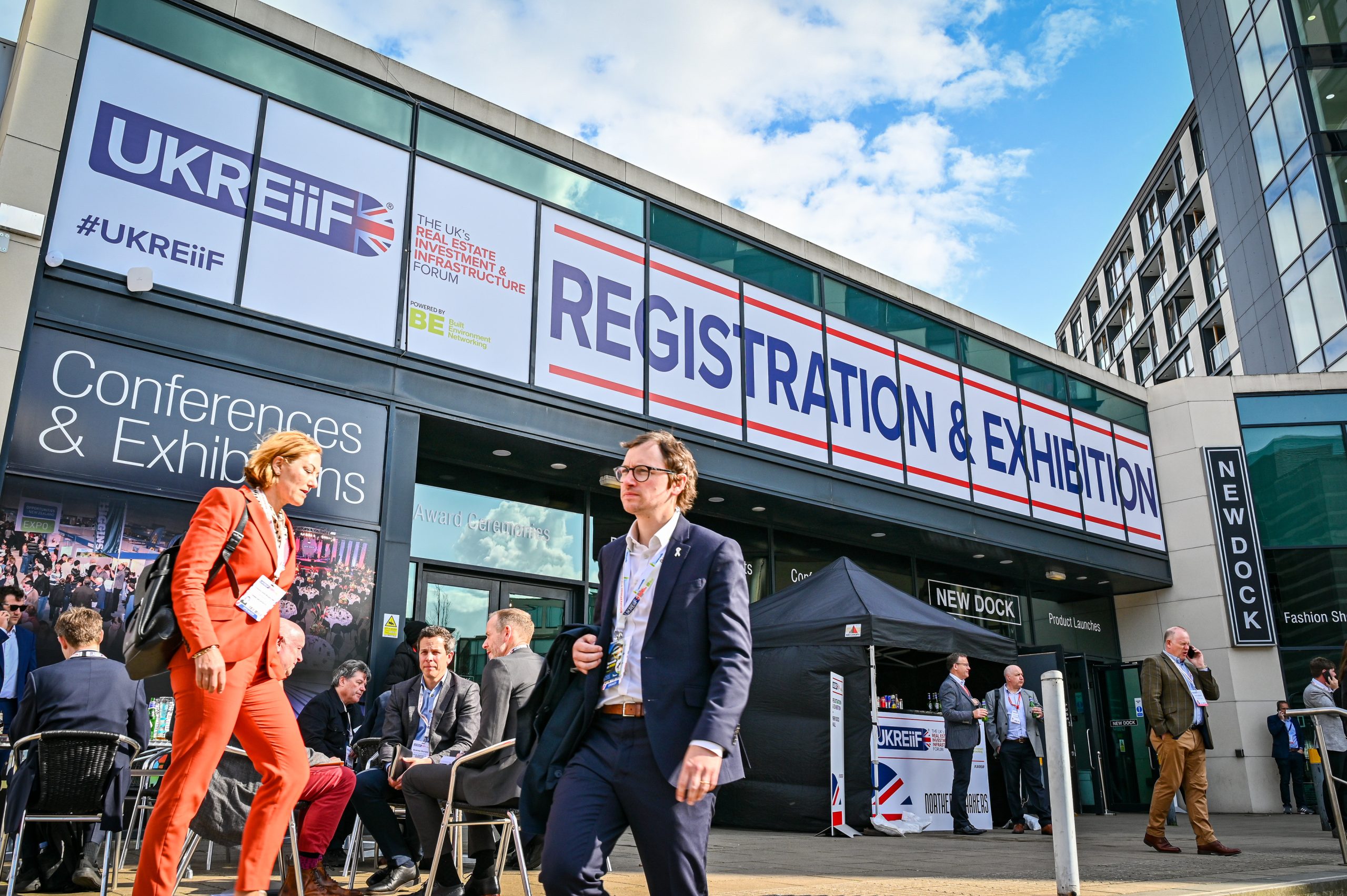 External shot of the UKREiiF-branded exhibition hall in Sheffield with people walking along outside the building