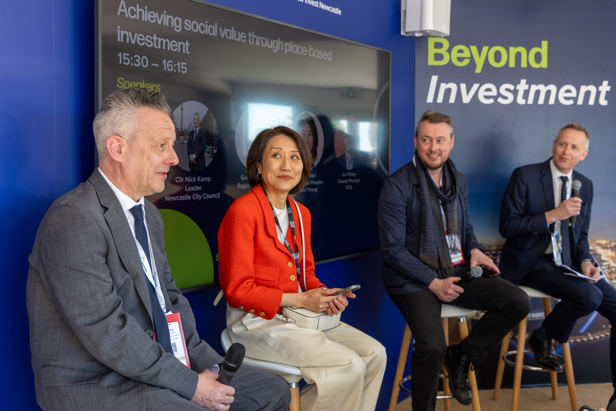 Four people sat on stools in front of room on a panel in the Newcastle stand at MIPIM presenting the audience.