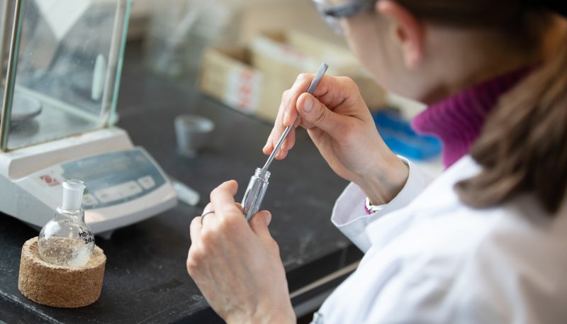 An over-the-shoulder shot of a person in a laboratory removing something from a vile with tweezers