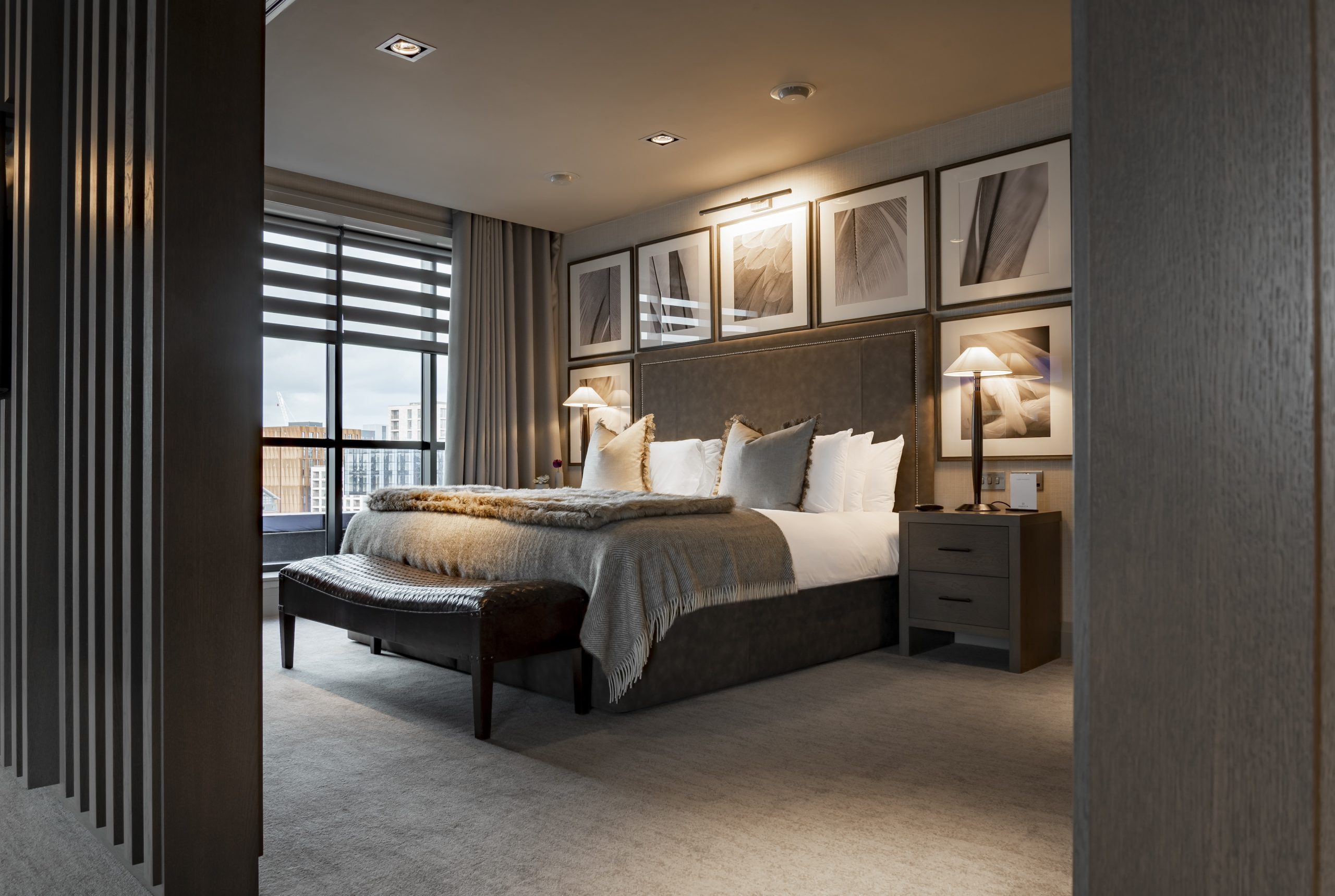 Grey and white themed hotel room with large double bed framed by large square photo frames and window to the left of the bed,