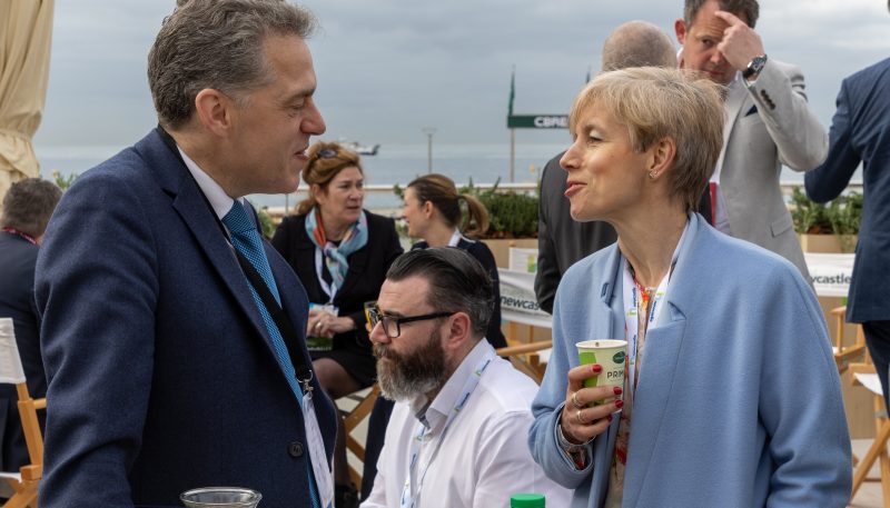 Two people stood on outside terrace at MIPIM networking together. One person is holding a coffee cup.