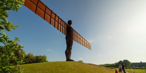 Image of Angel of the North statue on a grassy hill against a blue sky.