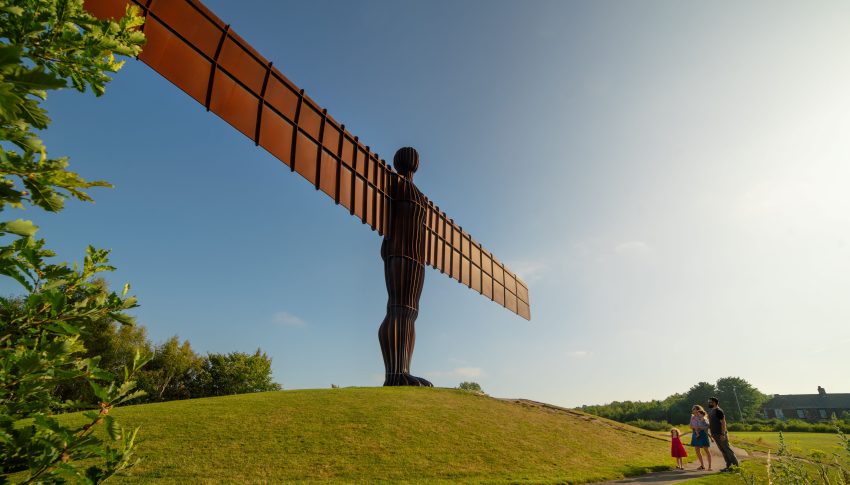 Image of Angel of the North statue on a grassy hill against a blue sky.