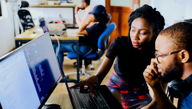 Two people looking at a laptop and computer screen together in discussion.
