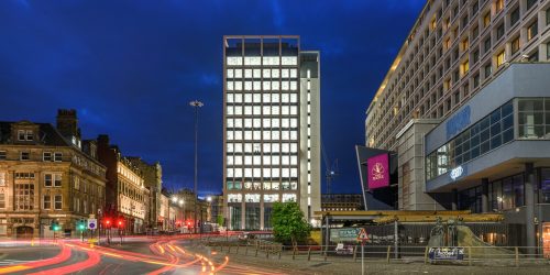 Image of Bank House office building at night with traffic speeding past in the foreground.