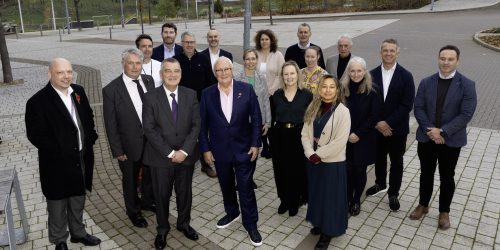 Group of stakeholders in business attire stood in vacant car park.