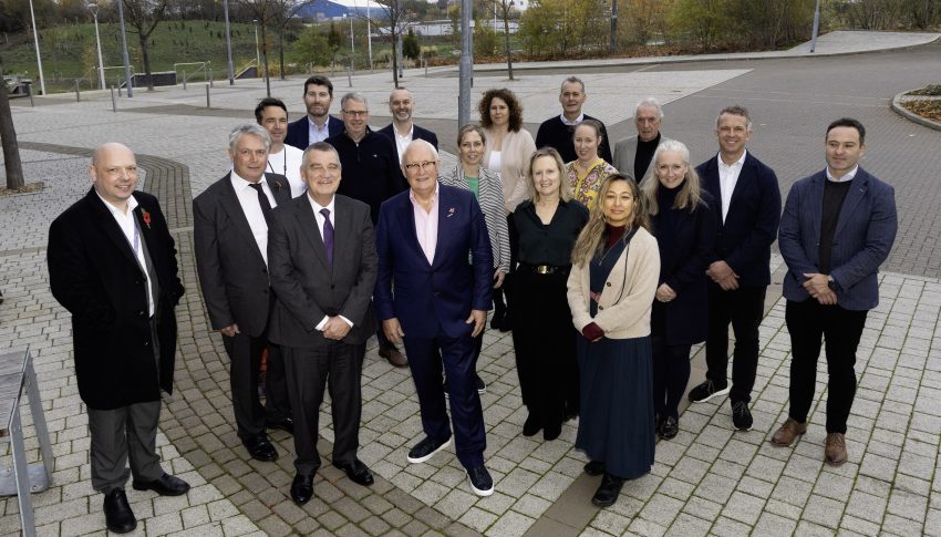 Group of stakeholders in business attire stood in vacant car park.