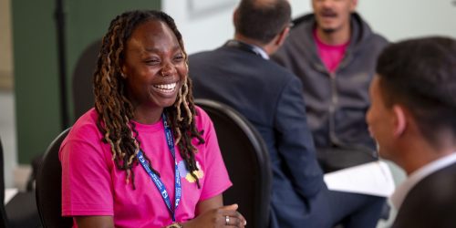 Young people smiling and talking together in a room wearing lanyards and holding sheets of paper.