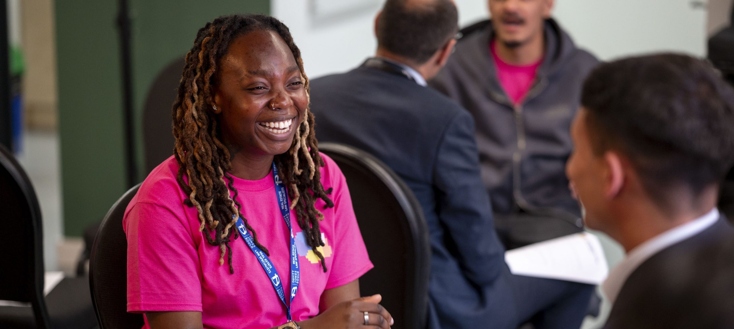 Young people smiling and talking together in a room wearing lanyards and holding sheets of paper.