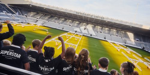 Children in the stands of St James' Park wearing navy Adidas t-shirts made specifically for the Mercury Prize Fringe.