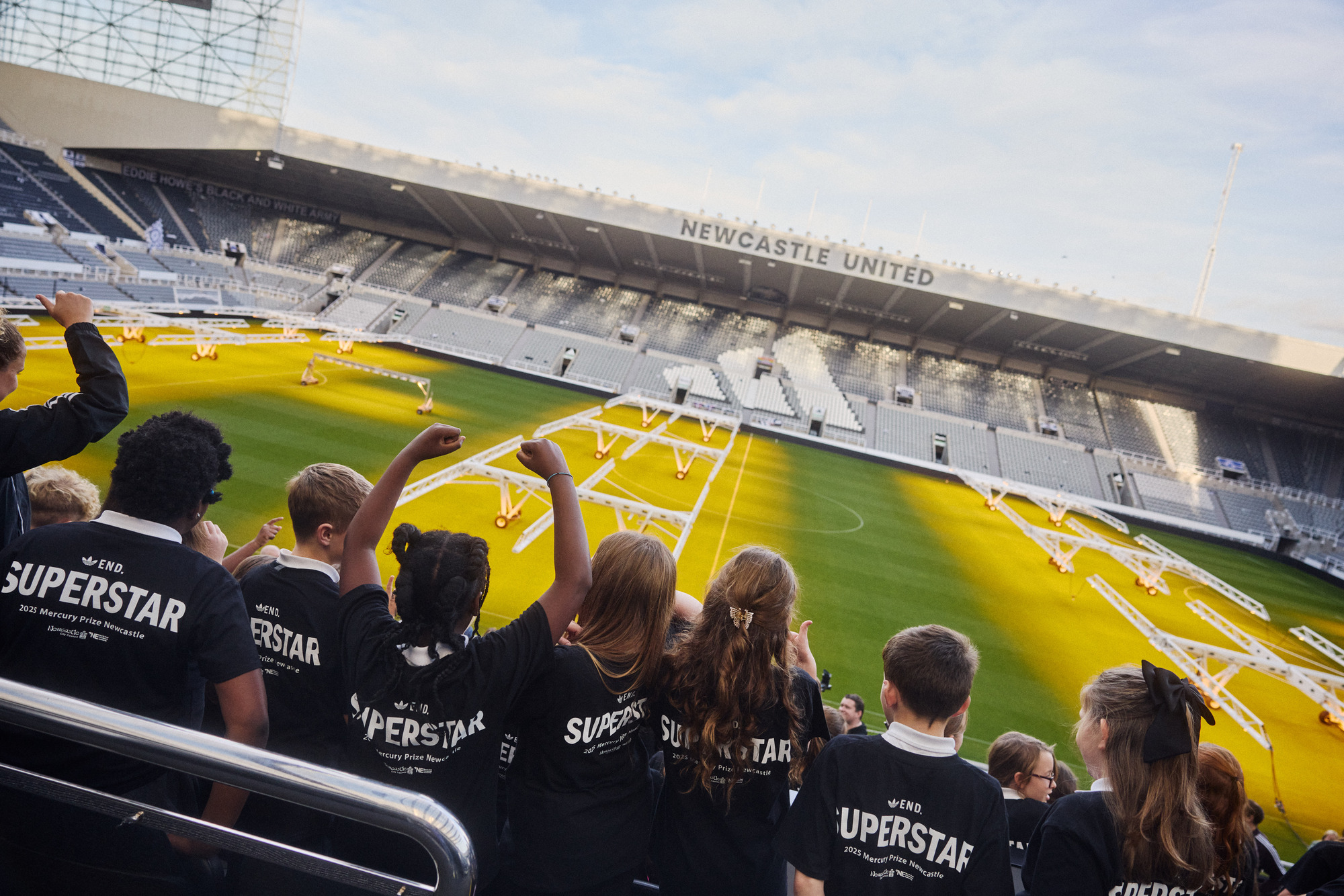 Children in the stands of St James' Park wearing navy Adidas t-shirts made specifically for the Mercury Prize Fringe.