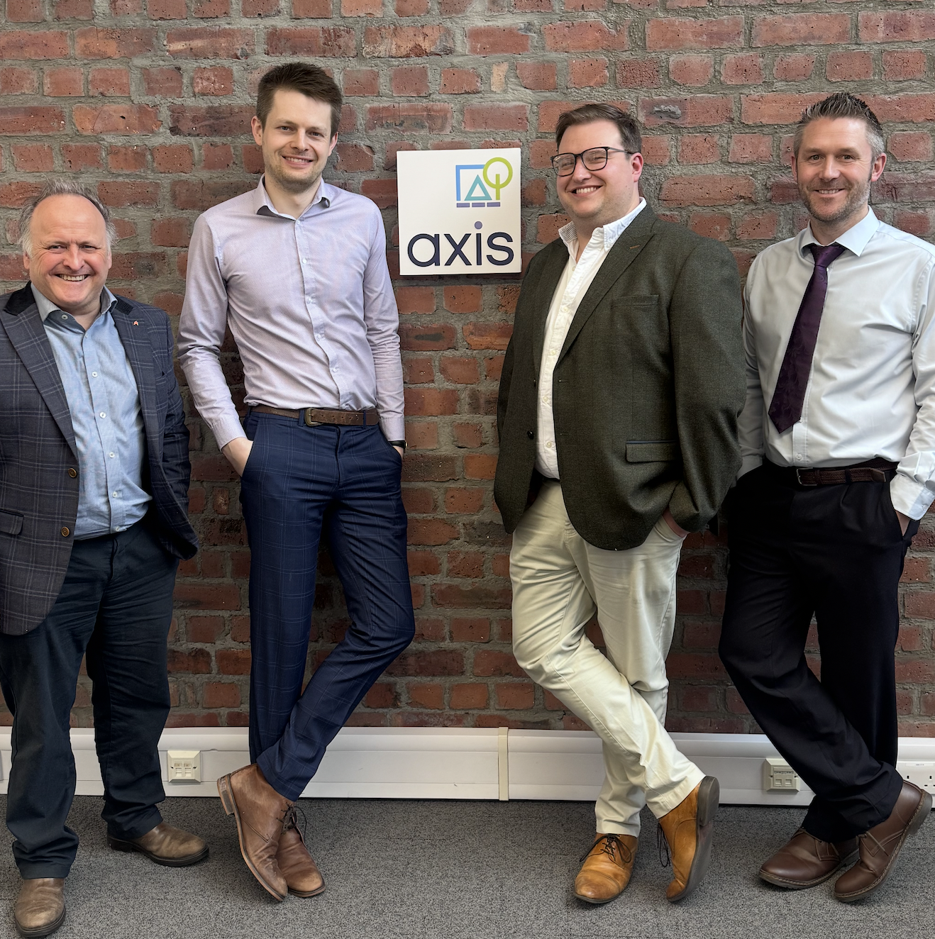 Four Axis Newcastle staff standing against brick wall with Axis branded sign in the middle.