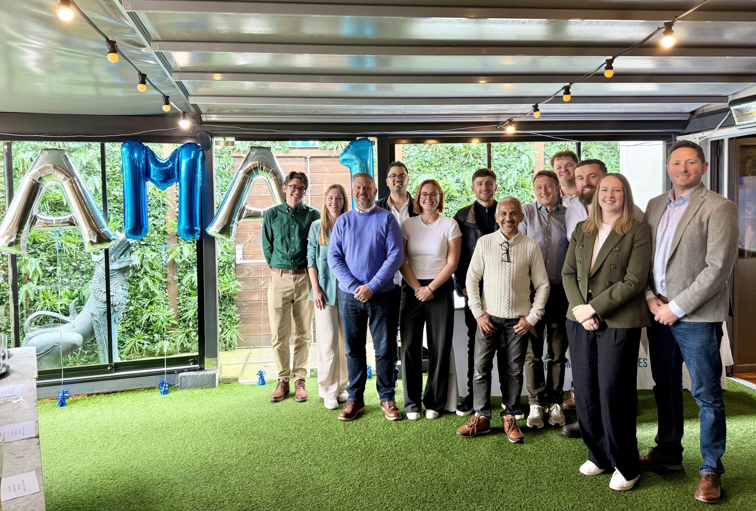 AMA team stood to the right smiling to camera with an AMA balloon banner to the left.